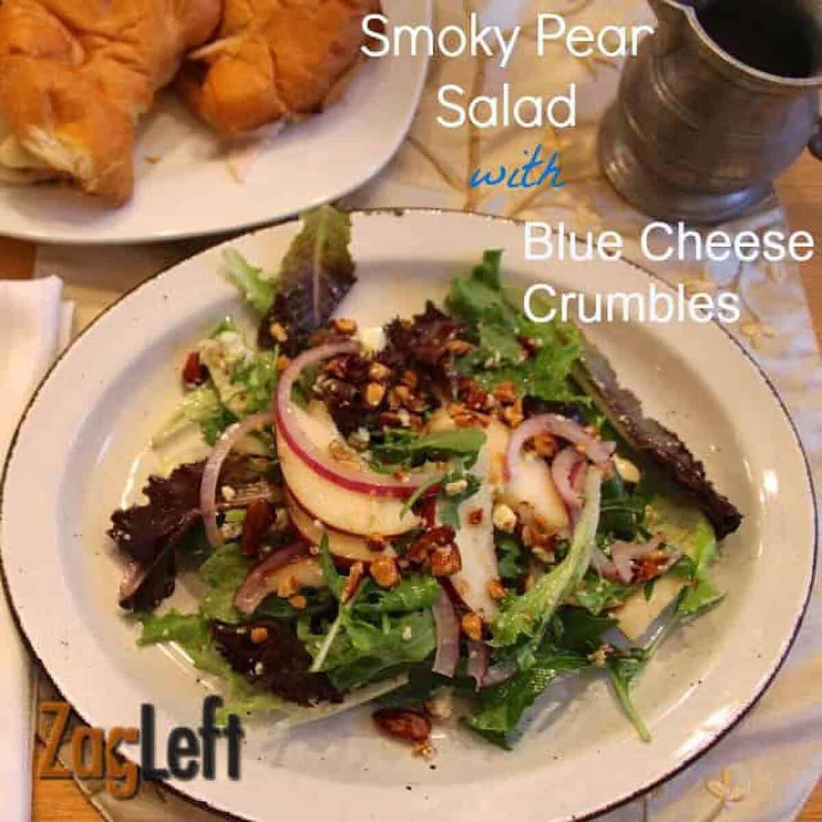 A plate of Smoky Pear Salad topped with Blue Cheese Crumbles and chopped almonds next to a plate of croissants
