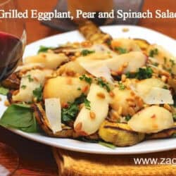 A plate of Grilled Eggplant, Pear and Spinach Salad topped with pine nuts and shaved asiago next to a glass of red wine