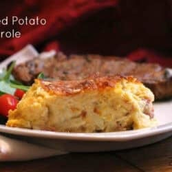 A slice of Loaded Potato Casserole on a plate with a steak and a side salad of spinach and cherry tomatoes