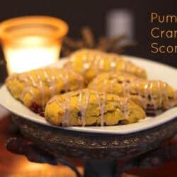 Four Pumpkin Cranberry Scones drizzled with glaze on a square plate with a candle in the background