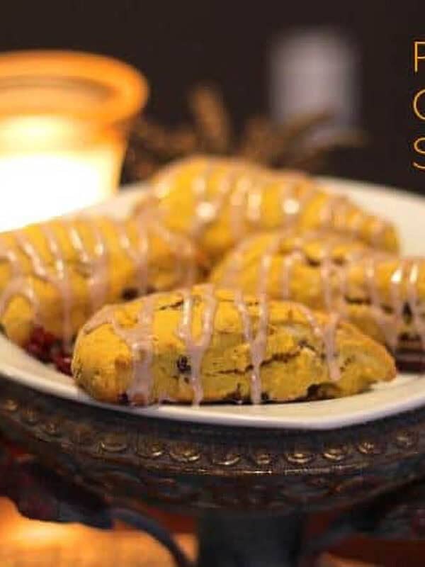 Four Pumpkin Cranberry Scones drizzled with glaze on a square plate with a candle in the background