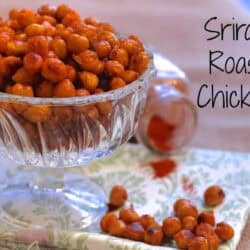 Sriracha Roasted Chickpeas in a dessert glass on a green and white patterned cloth napkin next to scattered sriracha chickpeas