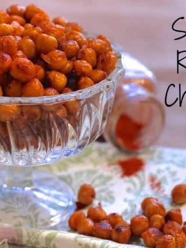 Sriracha Roasted Chickpeas in a dessert glass on a green and white patterned cloth napkin next to scattered sriracha chickpeas