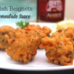 Five Crawfish Beignets on a plate with lemon slices next to a glass of Remoulade Sauce and a bottle of beer with a pool in the background