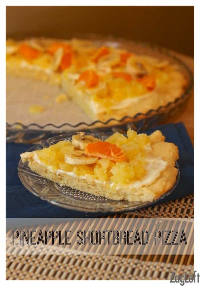 A slice of Pineapple Shortbread Pizza topped with banana slices and Mandarin orange slices on a small plate with the remainder of the pizza in the background