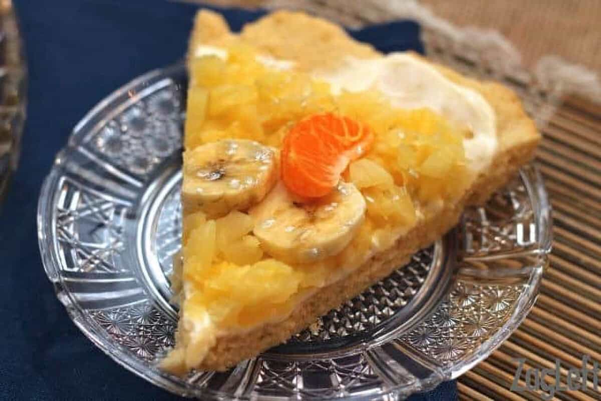 A slice of Pineapple Shortbread Pizza topped with two banana slices and a slice of Mandarin orange on a small plate