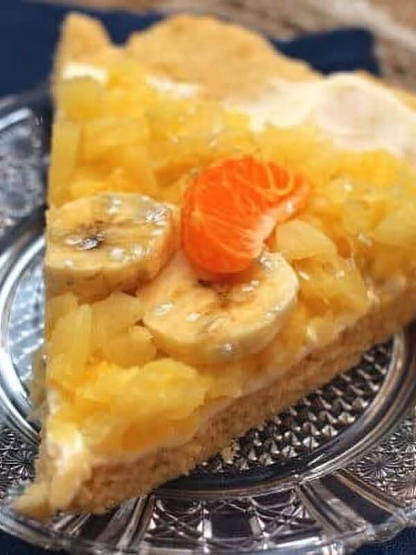 A slice of Pineapple Shortbread Pizza topped with two banana slices and a slice of Mandarin orange on a small plate
