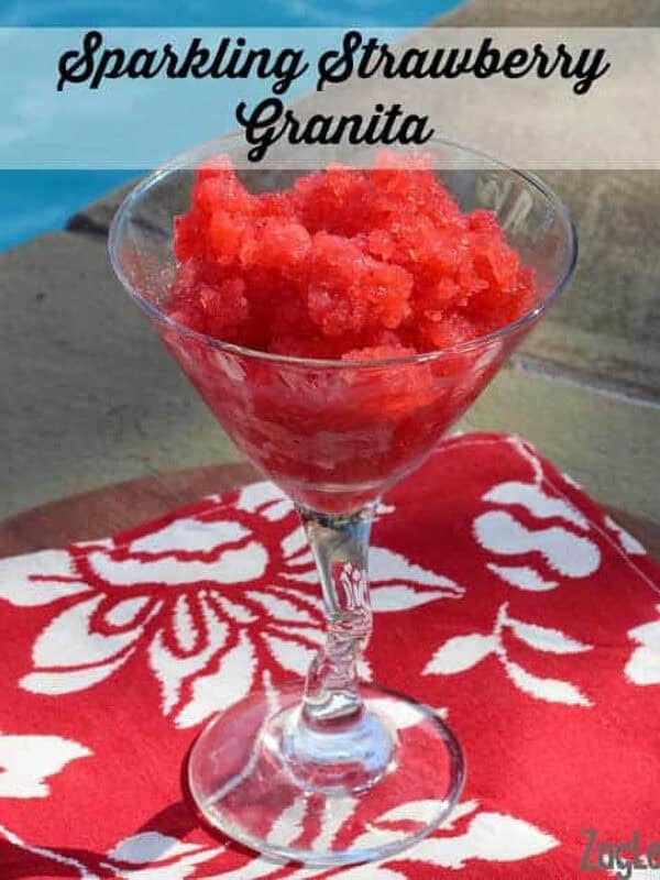 Sparkling Strawberry Granita in a tall dessert glass on a red cloth napkin with a pool in the background