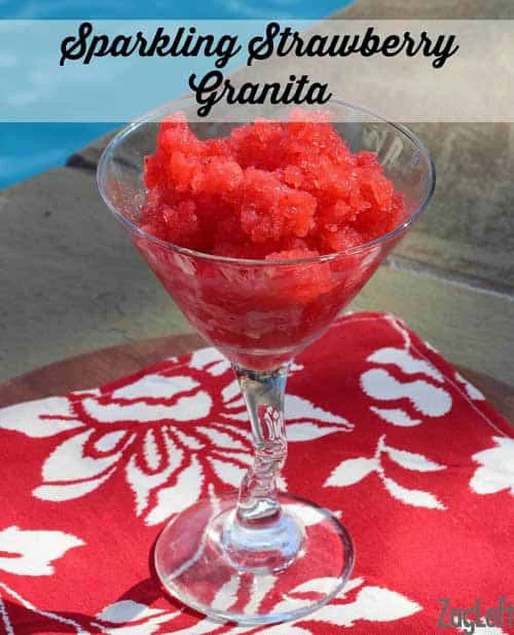 Sparkling Strawberry Granita in a tall dessert glass on a red cloth napkin with a pool in the background