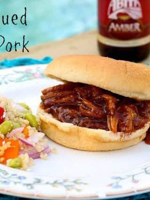 Hamburger bun with pulled pork in red bbq sauce on a white plate.