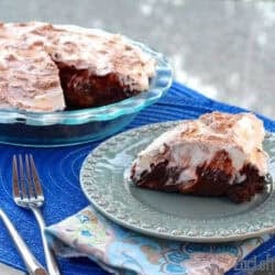 A slice of Double Chocolate and Caramelized Banana Cream Pie topped with whipped cream on a small plate with the remainder of the pie in a pie dish in the background next to a fork