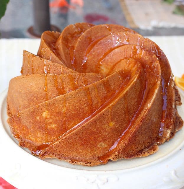 Orange Buttermilk Bundt Cake drizzled with orange glaze on a cake stand.