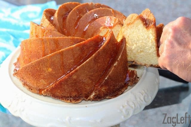 A cake server taking a slice out of a Orange Buttermilk Bundt Cake drizzled with orange glaze on a cake stand 