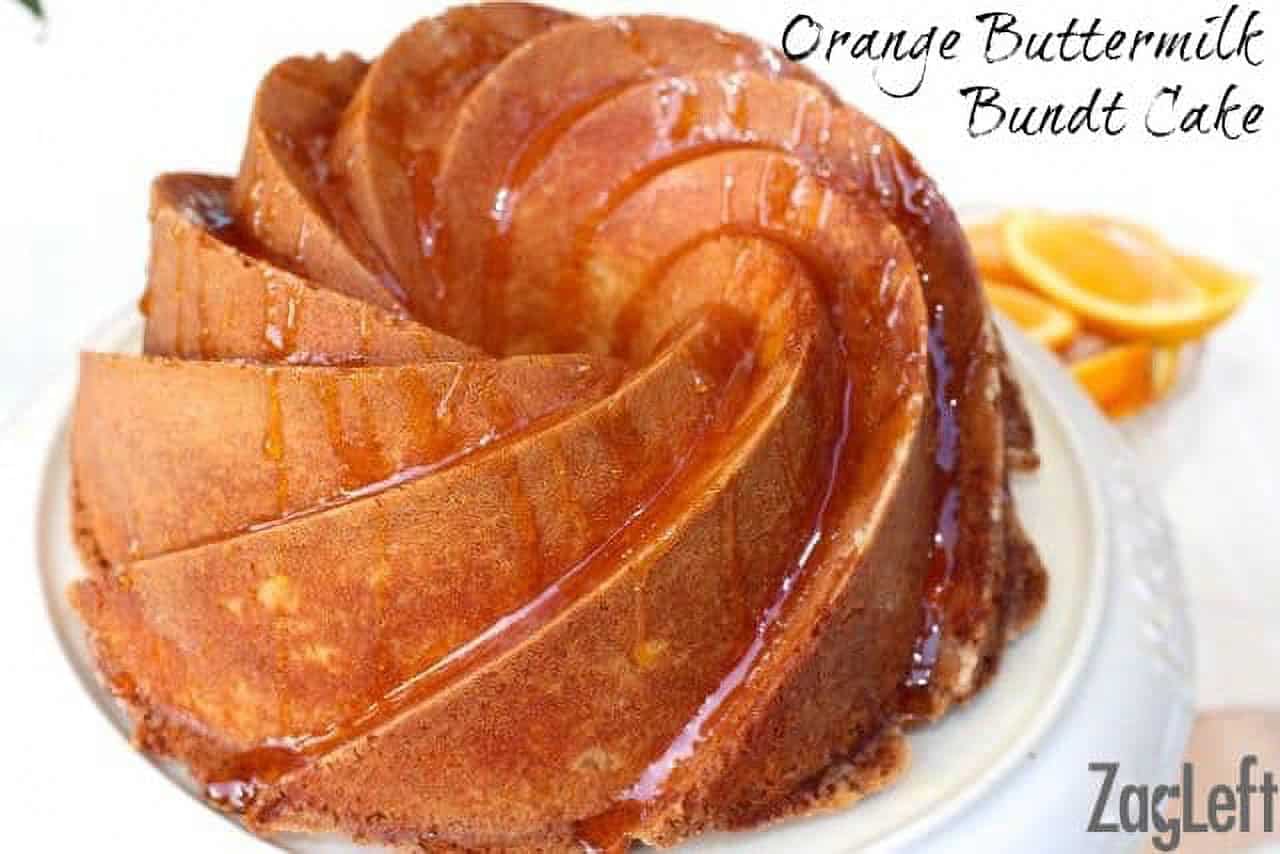 Orange Buttermilk Bundt Cake drizzled with orange glaze on a cake stand next to a small plate of orange slices.