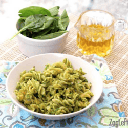 White bowl filled with rotini pasta covered with green pesto.