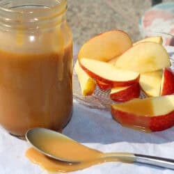 A small plate of apple slices next to a jar of salted caramel and a spoon