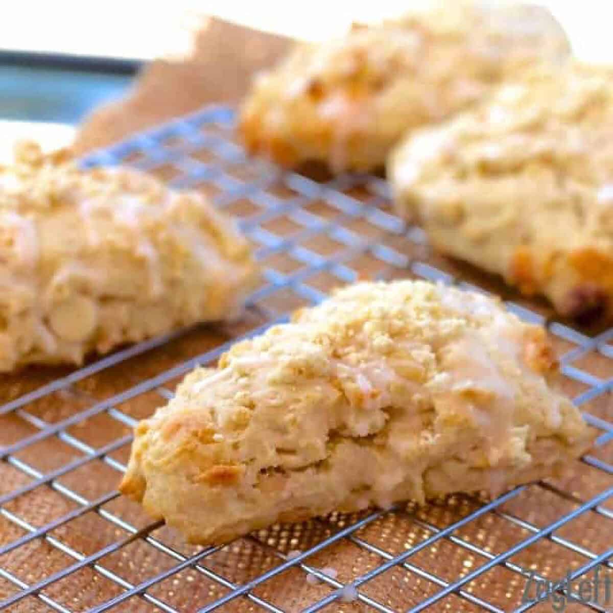 Four White Chocolate and Macadamia Nut Scones topped with glaze on a cooling rack