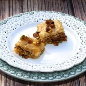 Two square slices of Baklava topped with pistachios on a large plate