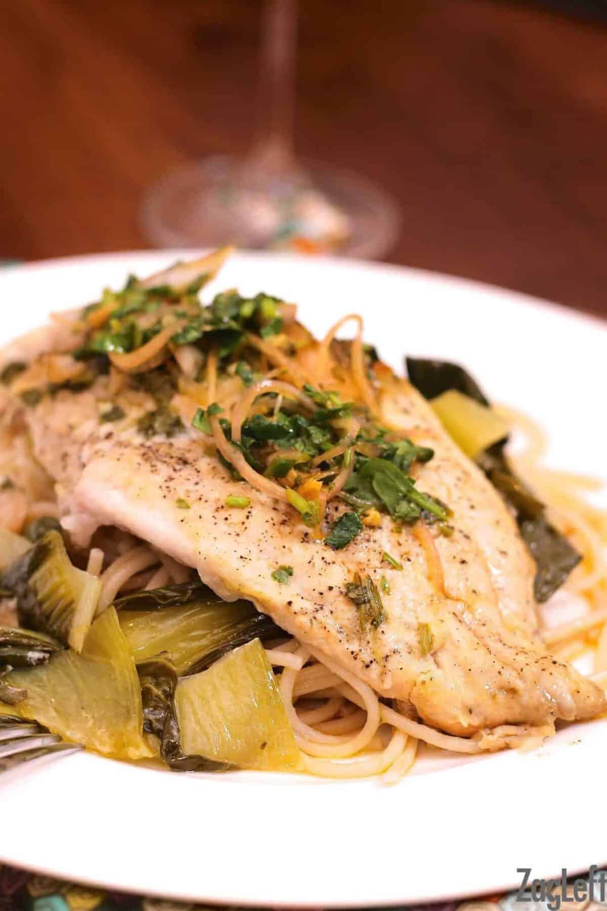 Catfish on a bed of Bok Choy and pasta and topped with Cilantro and Lime on a large plate 