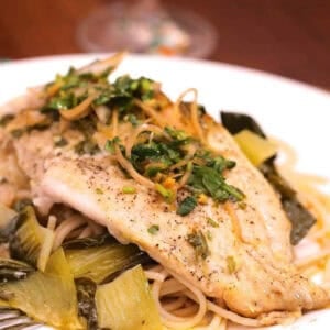 Catfish on a bed of Bok Choy and pasta and topped with Cilantro and Lime on a large plate