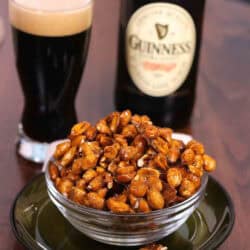 A small bowl of Guinness Glazed Nuts next to a bottle and a pint of Guinness