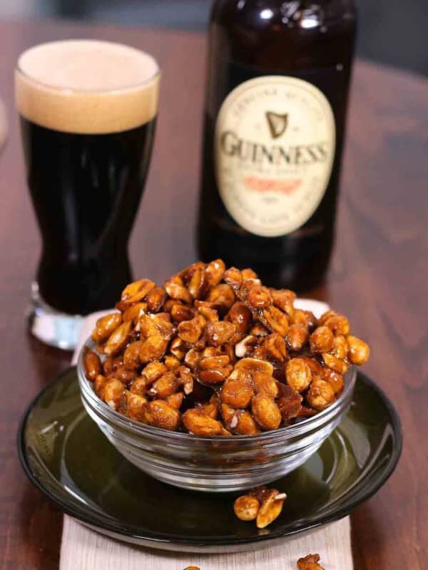 A small bowl of Guinness Glazed Nuts next to a bottle and a pint of Guinness