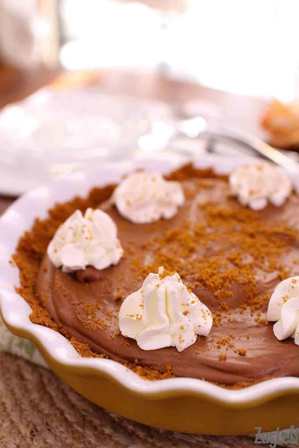 Chocolate Mousse Pie with Biscoff Crust topped with dollops of whipped cream and biscoff crumbles in a pie dish