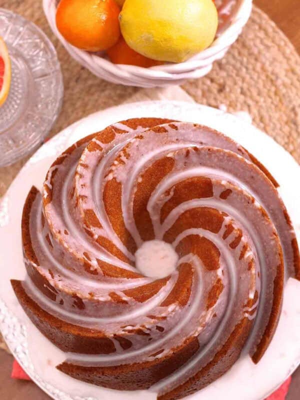 An overhead view of Lemon Grapefruit Buttermilk Cake topped with white icing next to a large bowl of grapefruits and oranges
