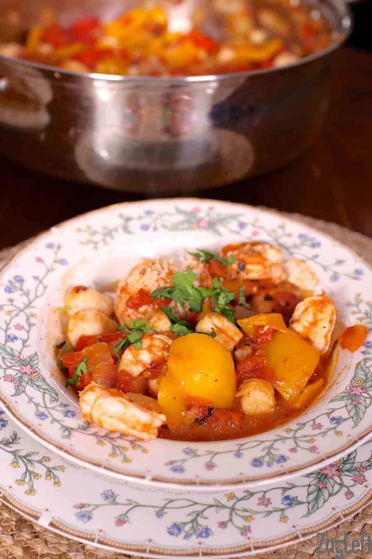 A bowl of Spicy Shrimp and Scallops next to a large pot with the remainder of the dish
