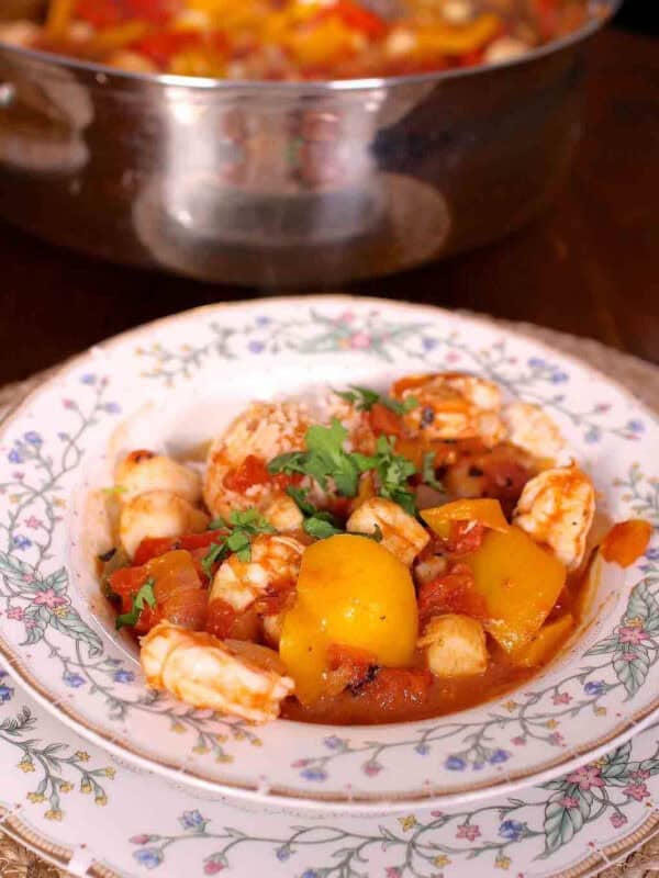 A bowl of Spicy Shrimp and Scallops next to a large pot with the remainder of the dish