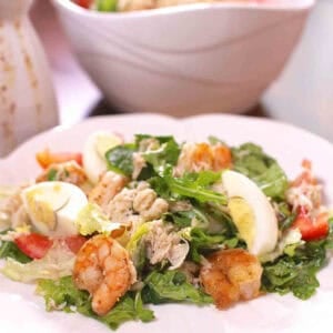 Shrimp and Crabmeat Salad topped with hard-boiled egg pieces on a large plate next to a serving bowl with the remainder of the salad