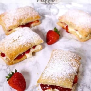 Four Strawberry Cheesecake Puffs dusted with powdered sugar next to a bowl of strawberries