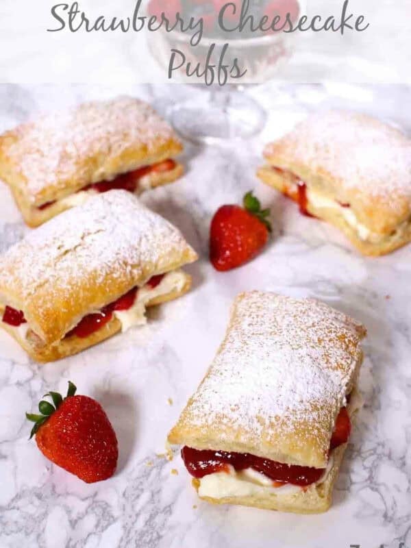 Four Strawberry Cheesecake Puffs dusted with powdered sugar next to a bowl of strawberries