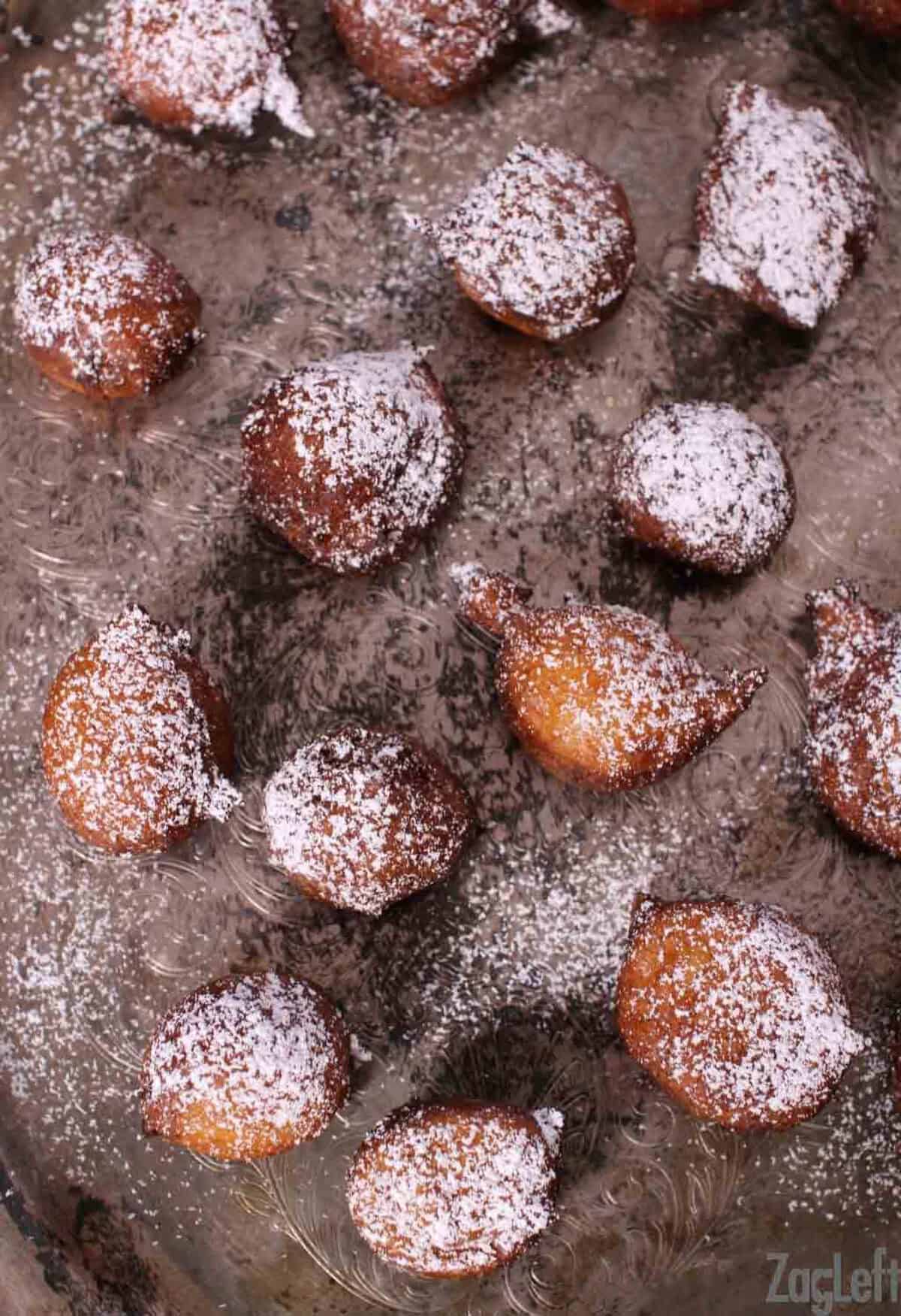 Overhead view of Zeppole di Ricotta donuts dusted with powdered sugar and scattered across a metal tray