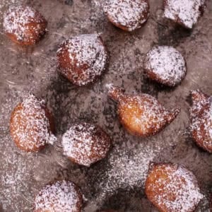 Overhead view of Zeppole di Ricotta donuts dusted with powdered sugar and scattered across a metal tray