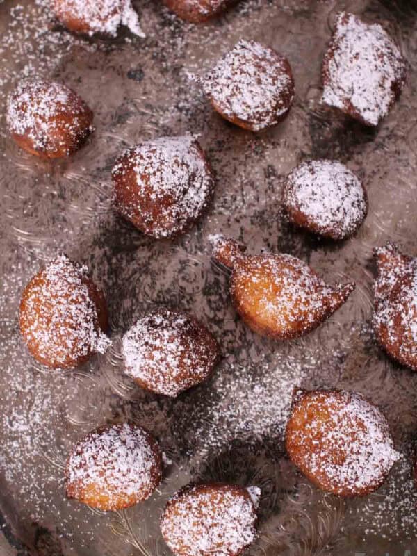 Overhead view of Zeppole di Ricotta donuts dusted with powdered sugar and scattered across a metal tray