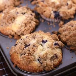 Six Blueberry Muffins with a buttery crumb topping in a muffin pan