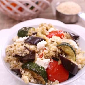 A bowl of Roasted Vegetable and Quinoa Salad next to a bowl of orange and yellow peppers and a measuring spoon on quinoa