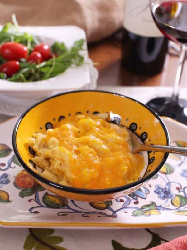 Three Cheese Macaroni and Cheese in a bowl next to a small salad and a glass of red wine