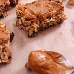 Square Dried Fruit Granola Bars topped with melted cinnamon chips on parchment paper next to a spoonful of melted cinnamon chips