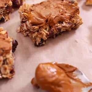 Square Dried Fruit Granola Bars topped with melted cinnamon chips on parchment paper next to a spoonful of melted cinnamon chips