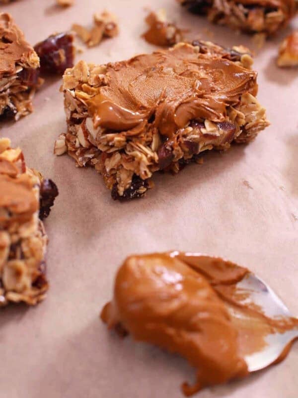Square Dried Fruit Granola Bars topped with melted cinnamon chips on parchment paper next to a spoonful of melted cinnamon chips
