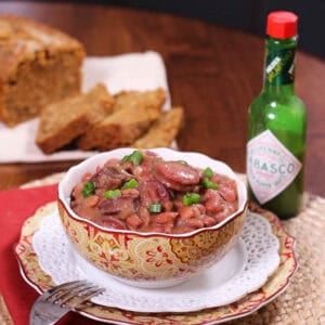 A bowl of Red Beans and Rice next to a bottle of hot sauce and a plate of beer bread