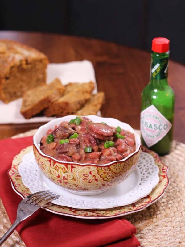 A bowl of Red Beans and Rice next to a bottle of hot sauce and a plate of beer bread