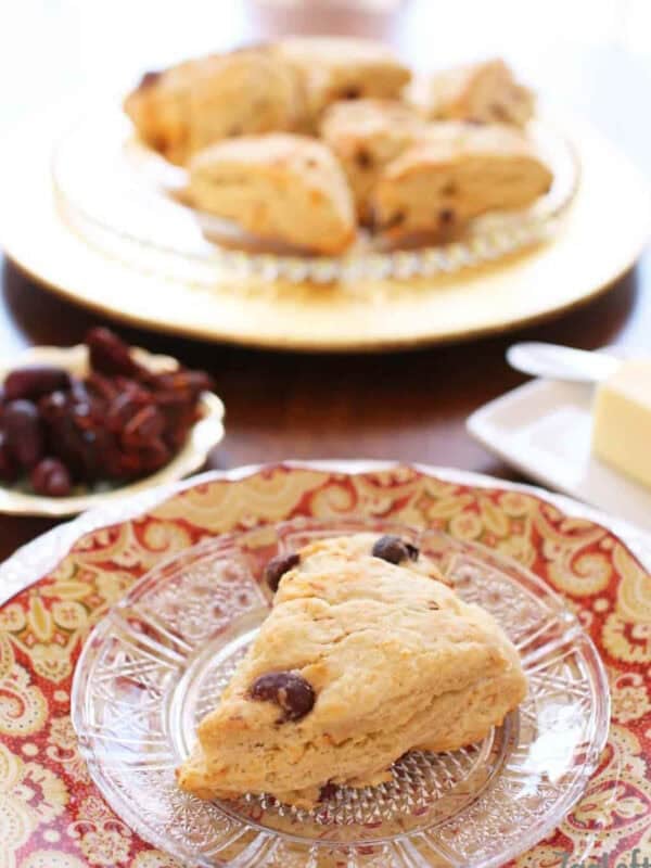 A buttery scone with sun-dried tomatoes, kalamata olives and crumbled goat cheese on a small plate with a batch of scones on a large plate in the background