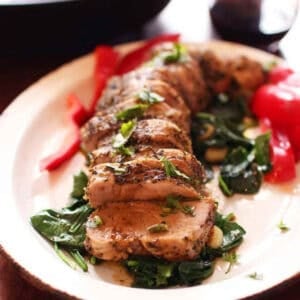 Sliced Herb Crusted Pork Tenderloin coated with a blend of Italian spices and minced garlic on a bed of spinach on a large plate
