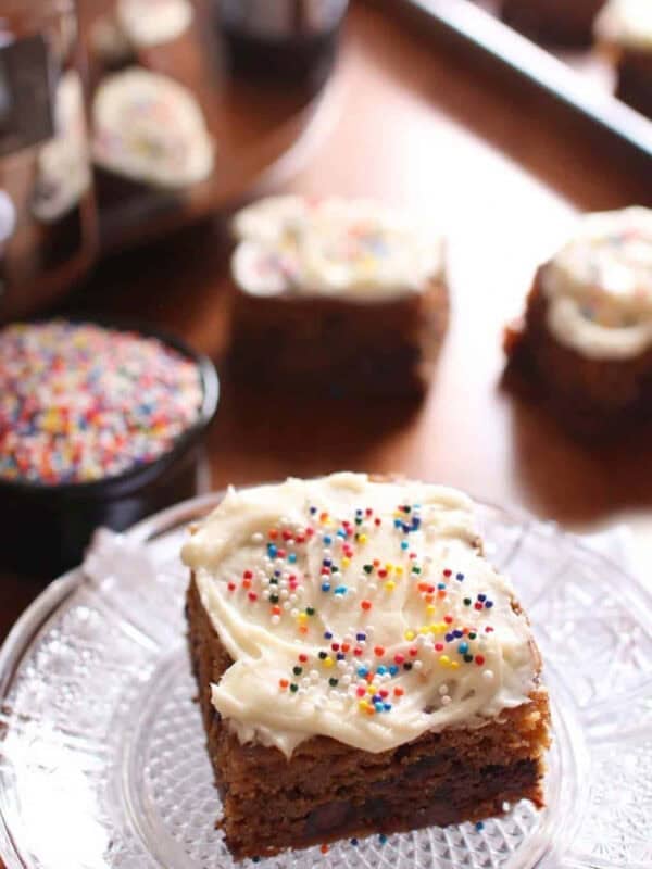 A slice of Frosted Chocolate Chip Cookie Bar with rainbow sprinkles on a small plate