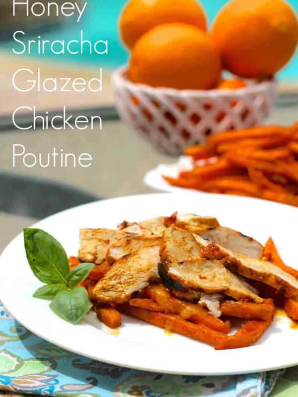 A plate of Honey Sriracha Glazed Chicken Poutine next to a bowl of oranges and a plate of sweet potato fries