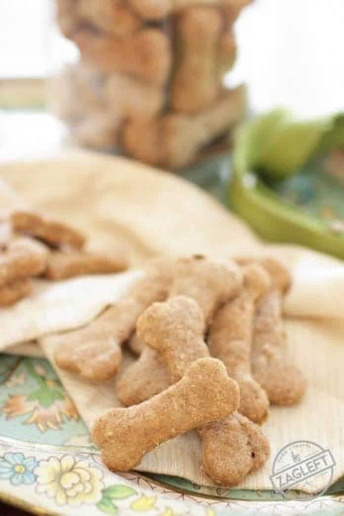 An overhead view of a jar of bone shaped dog treats on a metal tray next to a dog leash and scattered treats