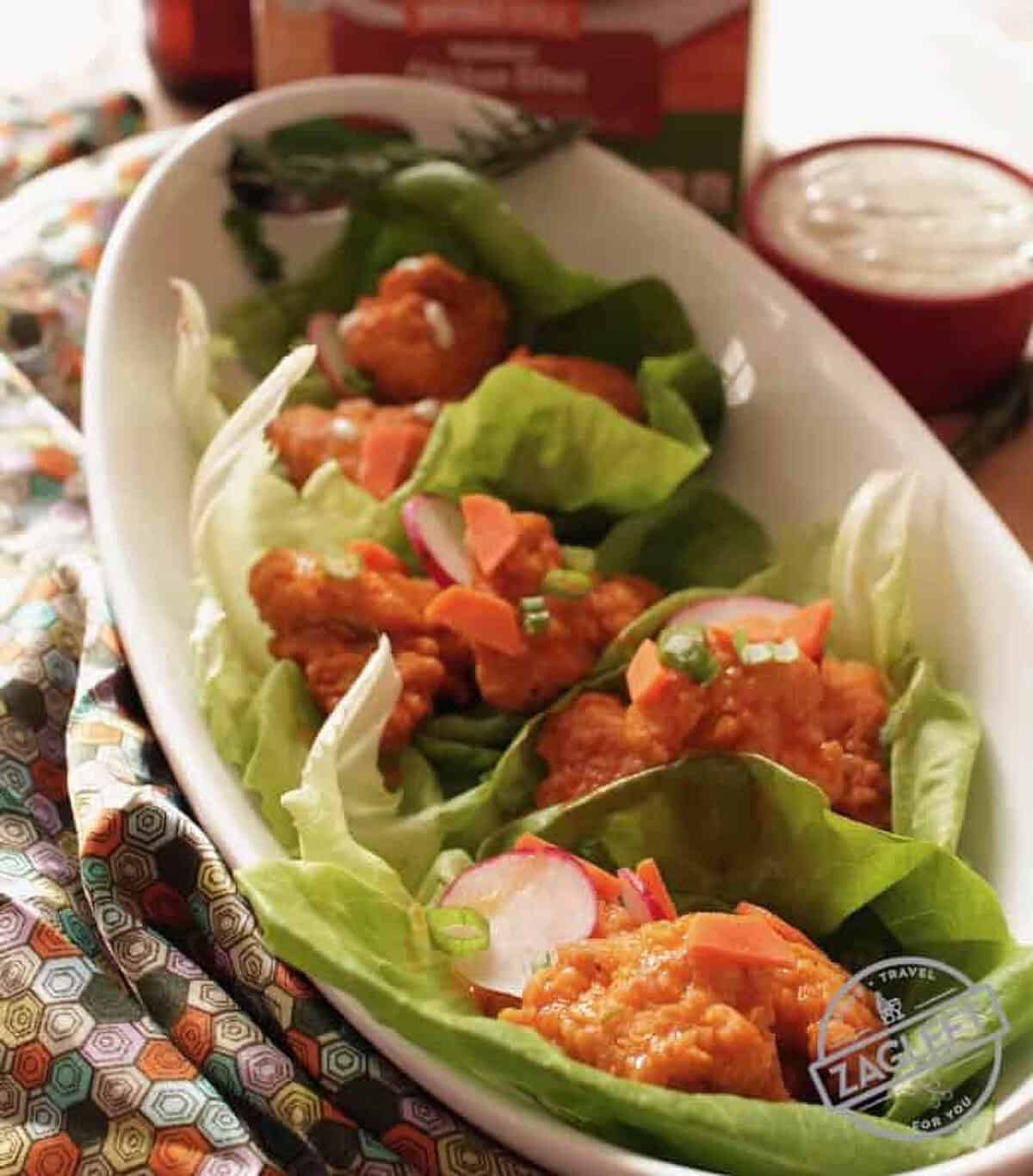 Baked Buffalo Chicken Lettuce Wraps in an oval dish next to a small bowl of ranch